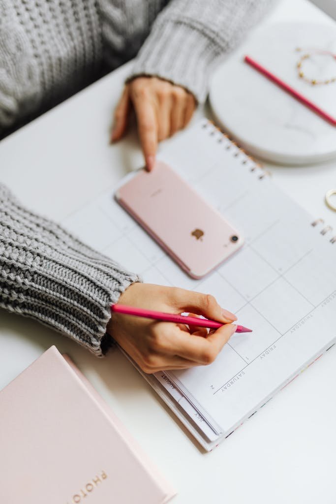 Close-up of a woman planning on a calendar using a smartphone and pen.